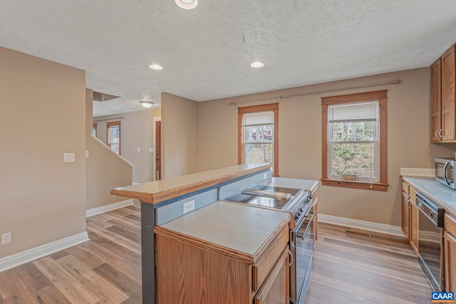 kitchen featuring stainless steel appliances, baseboards, light wood finished floors, a textured ceiling, and healthy amount of natural light