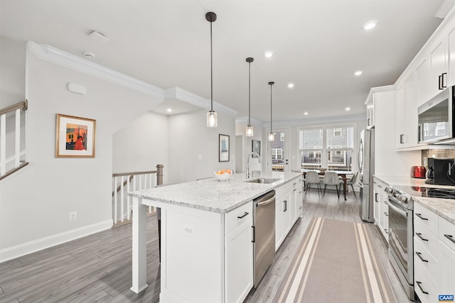 kitchen with stainless steel appliances, a sink, light wood-style flooring, a kitchen island with sink, and ornamental molding