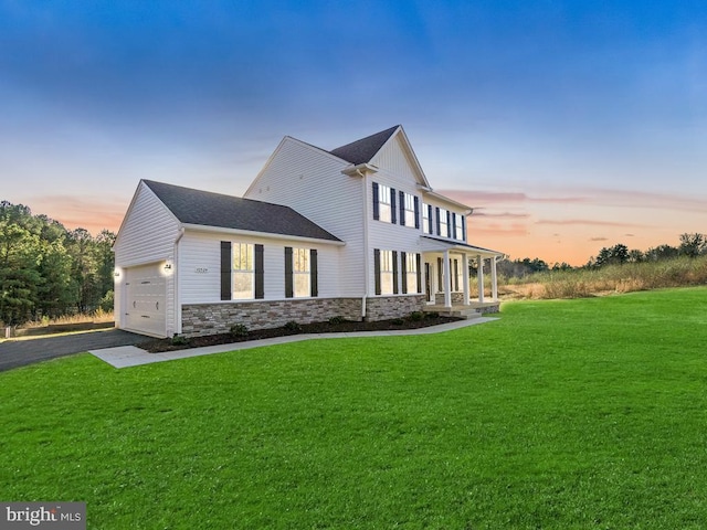 property exterior at dusk featuring a yard, stone siding, a porch, driveway, and an attached garage