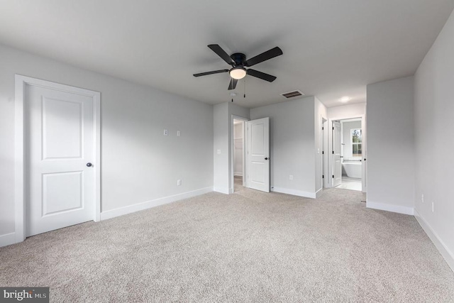unfurnished bedroom featuring baseboards, light colored carpet, ensuite bathroom, and ceiling fan