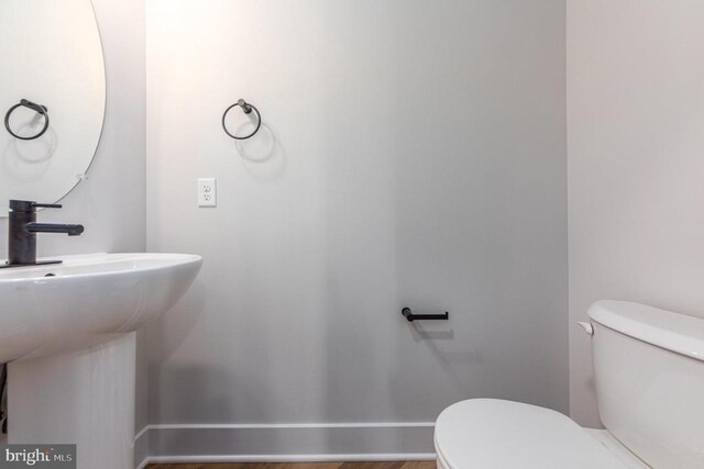 half bathroom featuring toilet, baseboards, and a sink