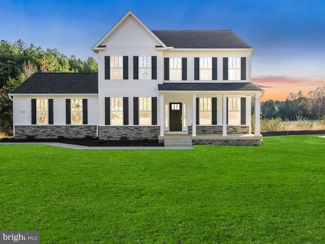 view of front facade with a lawn, stone siding, roof with shingles, and a porch