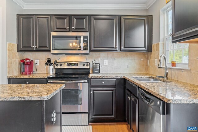 kitchen featuring a sink, stainless steel appliances, ornamental molding, light stone counters, and backsplash