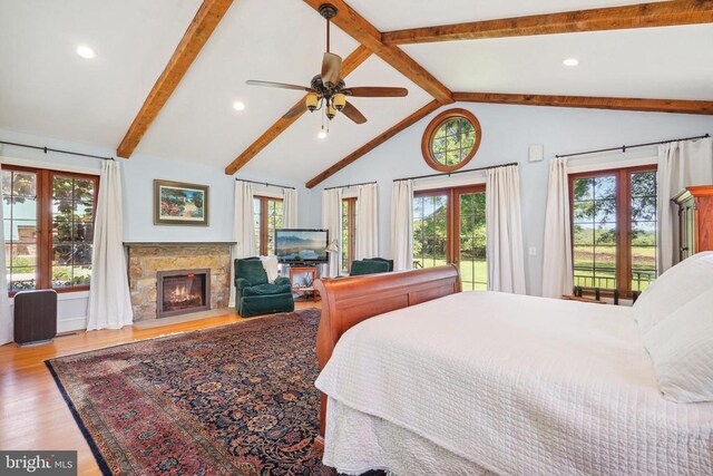 bedroom featuring access to outside, beamed ceiling, wood finished floors, multiple windows, and a glass covered fireplace