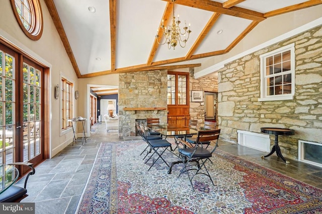 dining room featuring stone tile floors, french doors, high vaulted ceiling, a stone fireplace, and beamed ceiling