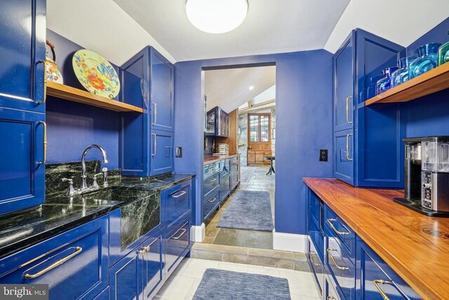kitchen featuring open shelves, wood counters, baseboards, blue cabinets, and lofted ceiling