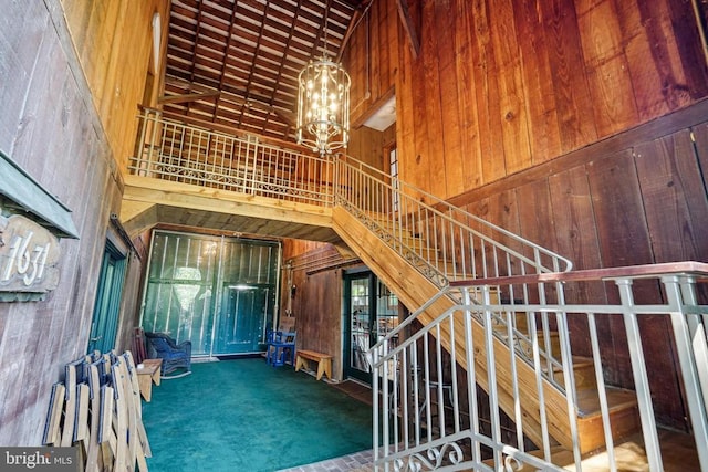 stairs with high vaulted ceiling, wood walls, a chandelier, and carpet floors