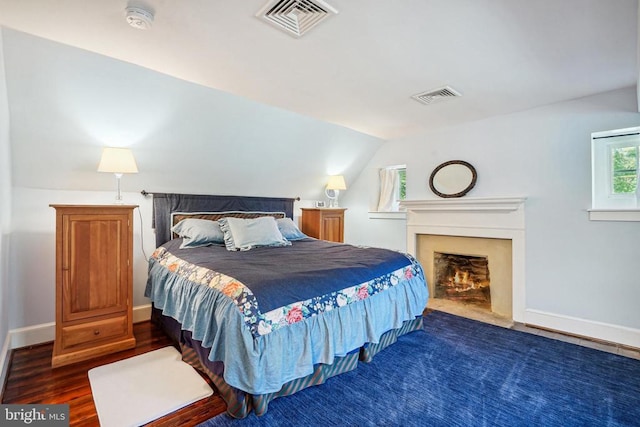 bedroom featuring baseboards, lofted ceiling, a lit fireplace, and wood finished floors