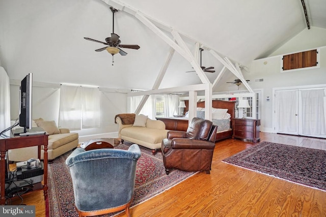living room with a ceiling fan, high vaulted ceiling, beam ceiling, wood finished floors, and baseboards