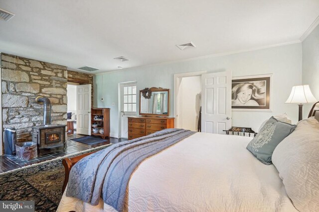 bedroom featuring a wood stove, crown molding, and wood finished floors