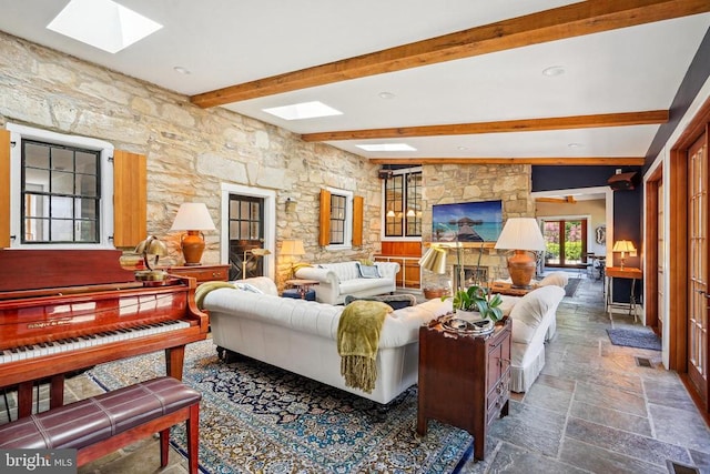 living room with a skylight, beamed ceiling, and stone tile floors