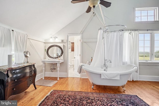 bathroom featuring healthy amount of natural light, wood finished floors, baseboards, a freestanding tub, and vaulted ceiling
