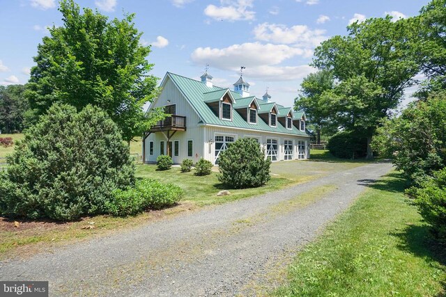 view of front facade featuring a balcony, metal roof, gravel driveway, and a front lawn