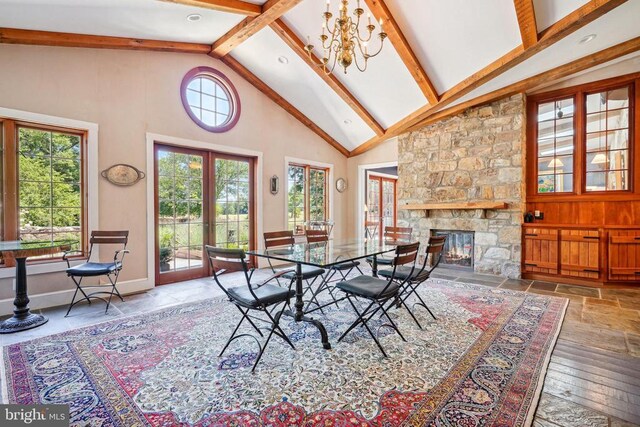 dining room featuring beam ceiling, high vaulted ceiling, a fireplace, baseboards, and stone tile floors