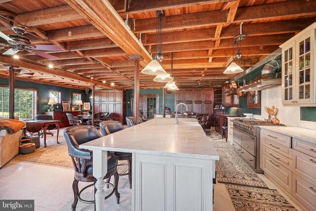 kitchen featuring high end stove, wood ceiling, wall chimney exhaust hood, a breakfast bar area, and open floor plan