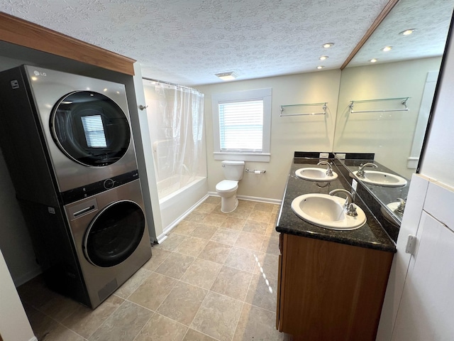 full bathroom featuring stacked washer and dryer, shower / bath combo, vanity, a textured ceiling, and toilet