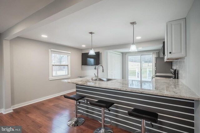kitchen with a sink, a peninsula, range, a kitchen bar, and light stone countertops