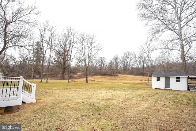view of grassy yard featuring an outbuilding, a wooden deck, a storage shed, and view of wooded area