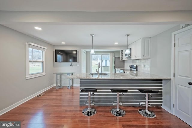 kitchen with a sink, stainless steel appliances, a peninsula, baseboards, and light stone counters