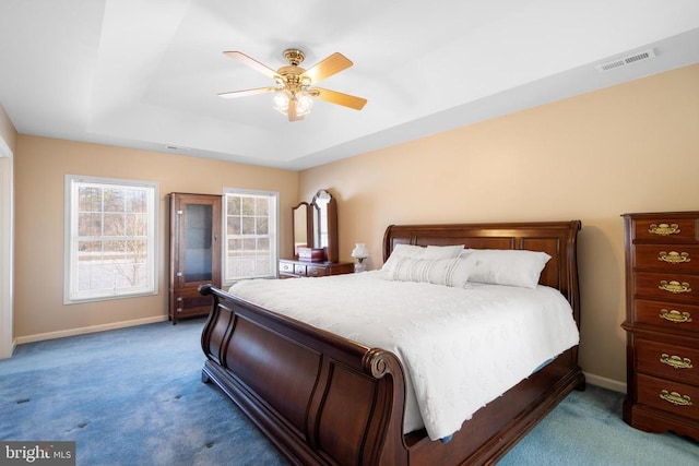 carpeted bedroom with ceiling fan, visible vents, baseboards, and a raised ceiling