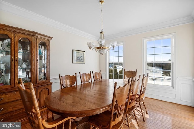 dining area with ornamental molding, light wood-type flooring, wainscoting, and an inviting chandelier