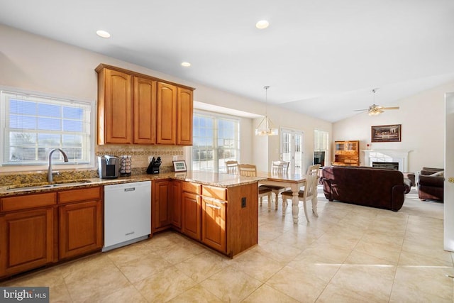 kitchen featuring white dishwasher, a peninsula, a fireplace, a sink, and light stone countertops