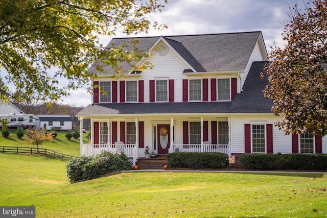 colonial house with a porch, a front yard, fence, and a shingled roof