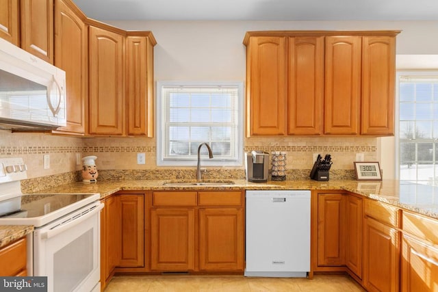 kitchen featuring white appliances, light stone counters, backsplash, and a sink