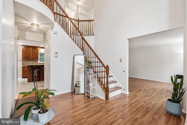  - stairway with a towering ceiling, ceiling fan, and wood finished floors