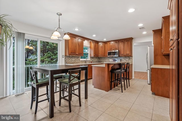  - kitchen featuring stainless steel appliances, backsplash, brown cabinetry, a center island, and a breakfast bar