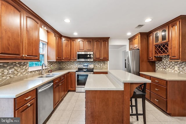  - kitchen with stainless steel appliances, light tile patterned flooring, a kitchen bar, decorative backsplash, and a kitchen island