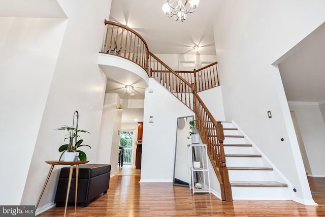  - stairs with a towering ceiling, wood finished floors, and a chandelier