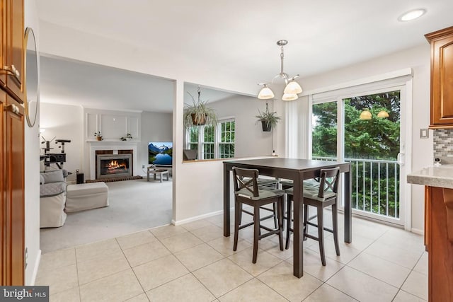 - dining area with light carpet, light tile patterned flooring, a fireplace, and a chandelier