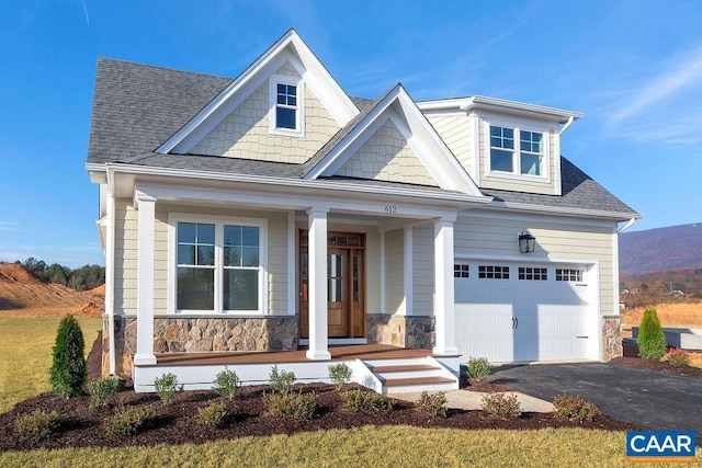 view of front of property featuring covered porch, stone siding, a garage, a shingled roof, and driveway