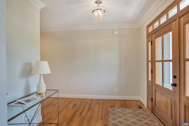 foyer entrance with visible vents, crown molding, light wood-style flooring, a notable chandelier, and baseboards
