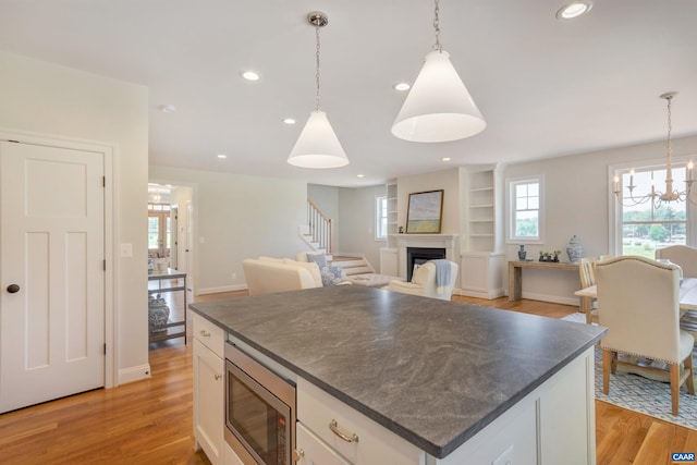 kitchen featuring dark countertops, light wood-type flooring, stainless steel microwave, and a notable chandelier