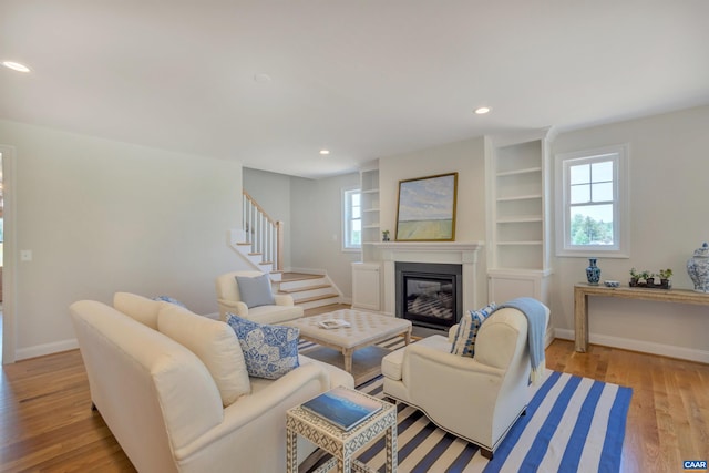 living area with stairway, baseboards, a glass covered fireplace, light wood-style floors, and recessed lighting