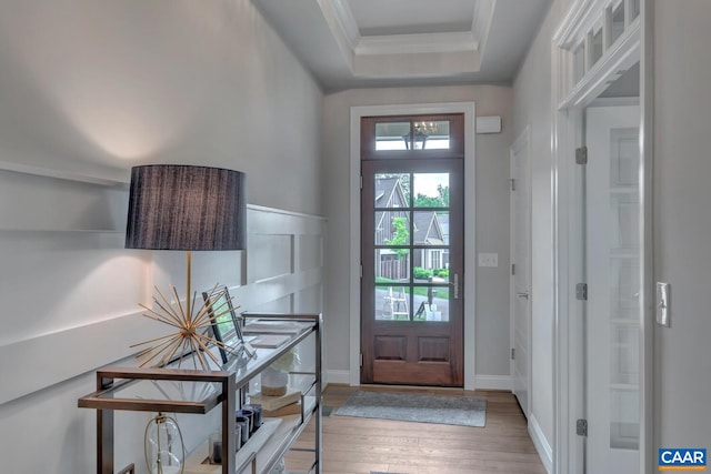 doorway to outside with a tray ceiling, crown molding, a chandelier, and wood finished floors