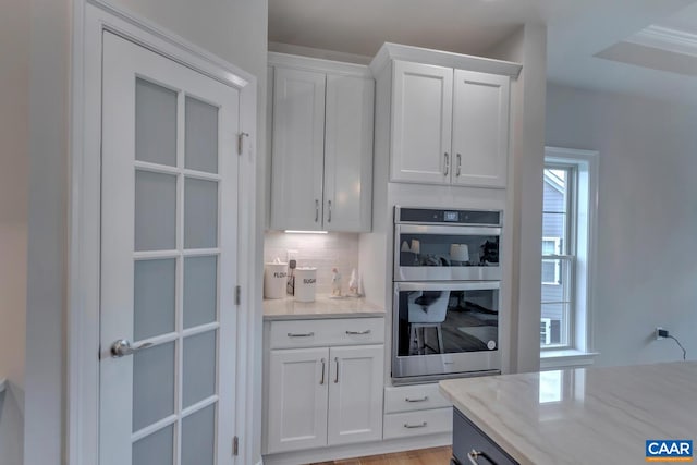kitchen with white cabinetry, light stone counters, decorative backsplash, and stainless steel double oven