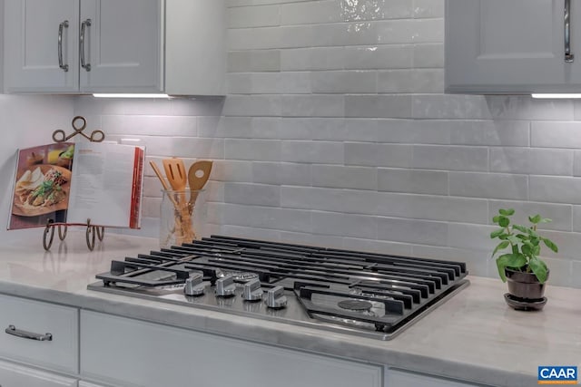 interior details with white cabinets, light countertops, stainless steel gas stovetop, and decorative backsplash