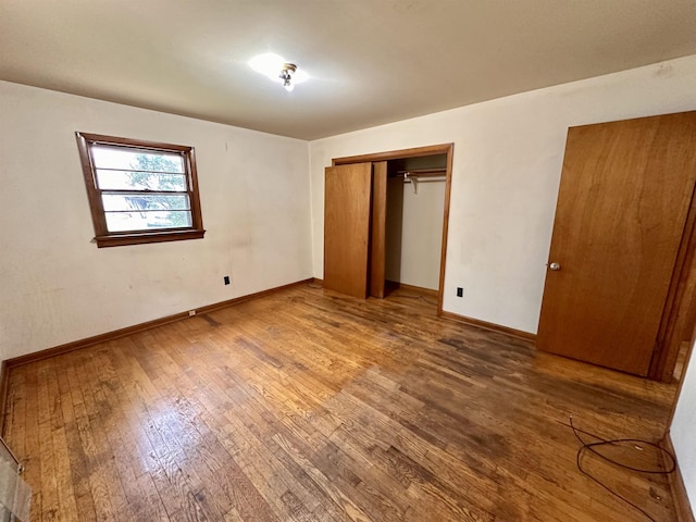 unfurnished bedroom featuring wood-type flooring, baseboards, and a closet