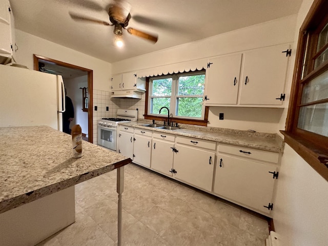 kitchen with white appliances, a sink, under cabinet range hood, and light countertops