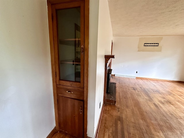 corridor featuring wood finished floors, a textured ceiling, and baseboards