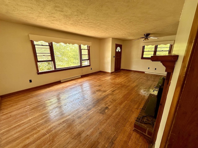 unfurnished living room with wood finished floors, a textured ceiling, plenty of natural light, ceiling fan, and baseboard heating