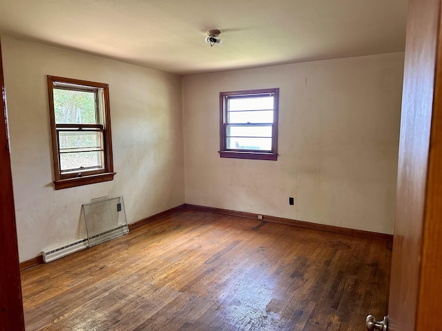 empty room featuring healthy amount of natural light, hardwood / wood-style floors, a baseboard heating unit, and baseboards
