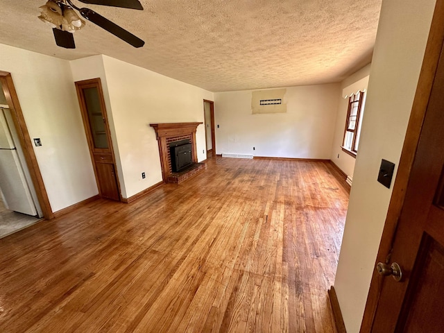 unfurnished living room with wood finished floors, a textured ceiling, a ceiling fan, a brick fireplace, and baseboards
