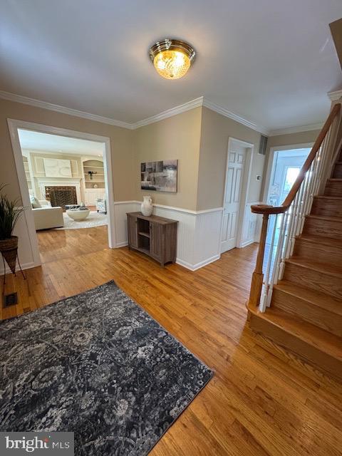  - living room with wood finished floors, ornamental molding, stairs, a wainscoted wall, and a fireplace