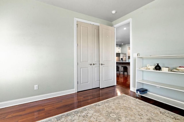 bedroom featuring wood finished floors, stainless steel refrigerator with ice dispenser, a closet, and baseboards