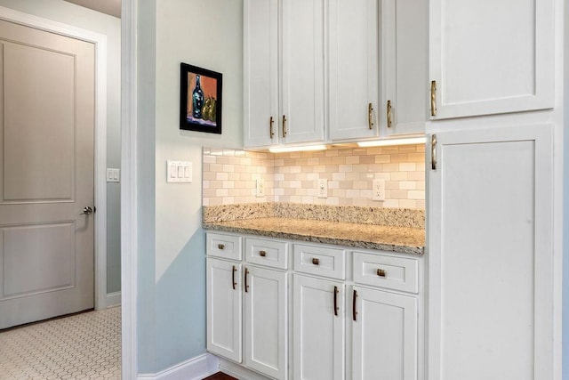 kitchen with white cabinetry, decorative backsplash, light stone counters, and baseboards