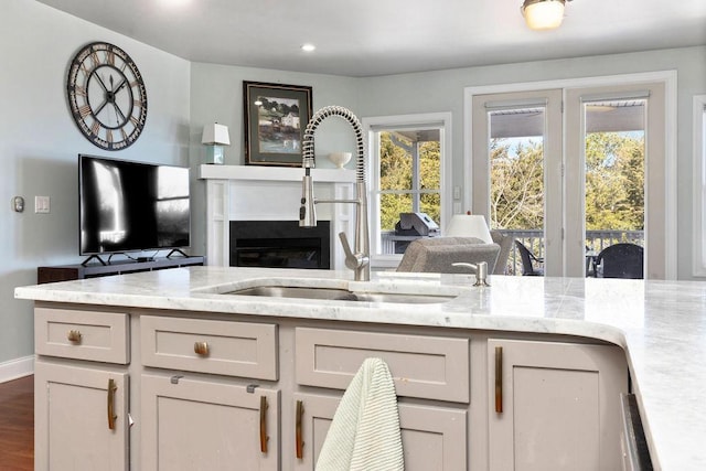 kitchen featuring a sink, a glass covered fireplace, open floor plan, light stone countertops, and dark wood-style flooring